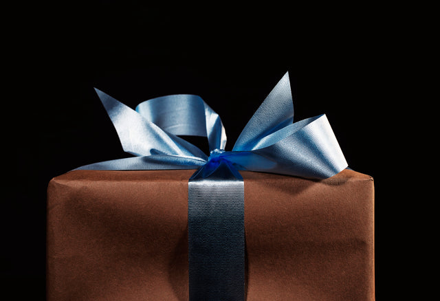 A brown paper wrapped present with a blue bow against a black background